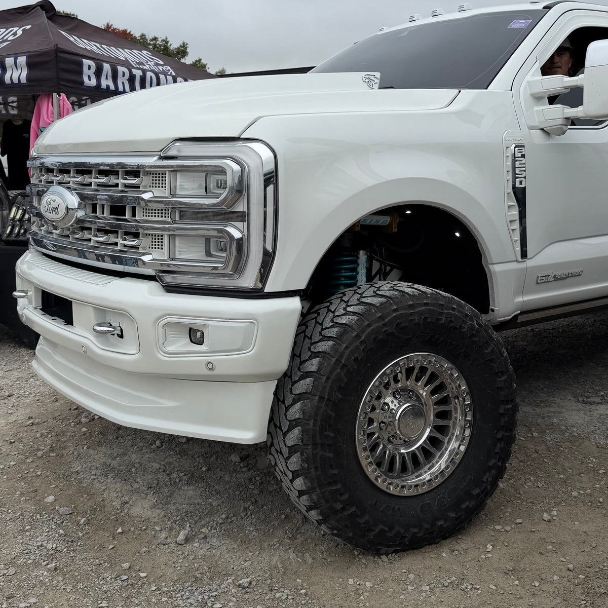 White Ford Super Duty pickup showing its polished multi-spoke wheel from another front angle.