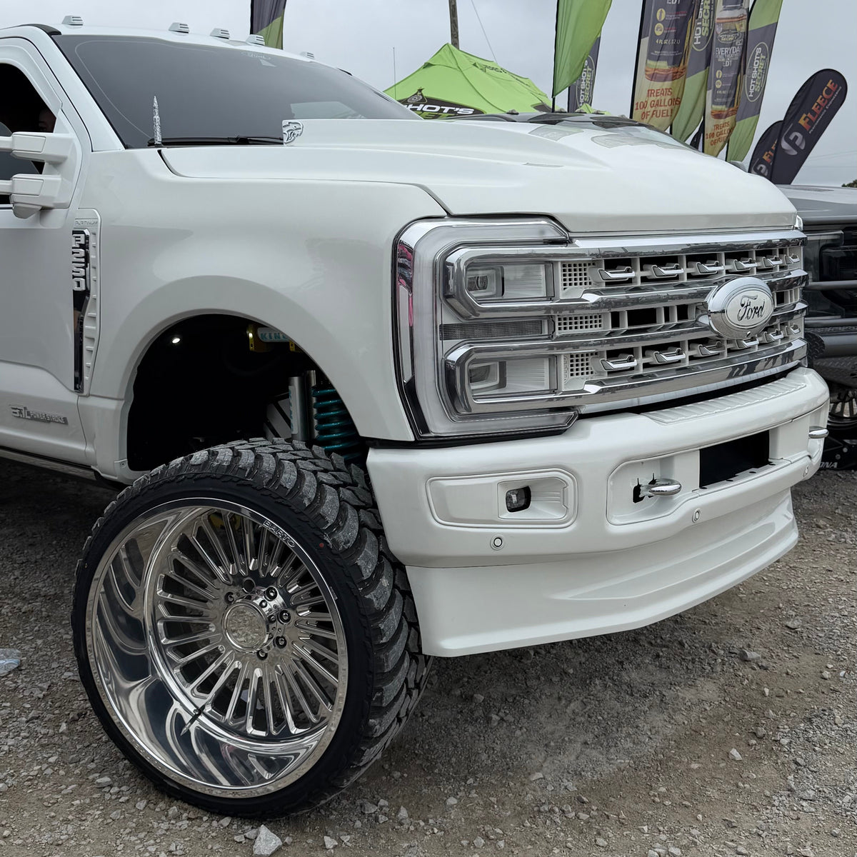 White Ford Super Duty pickup with polished multi-spoke wheels, front view.
